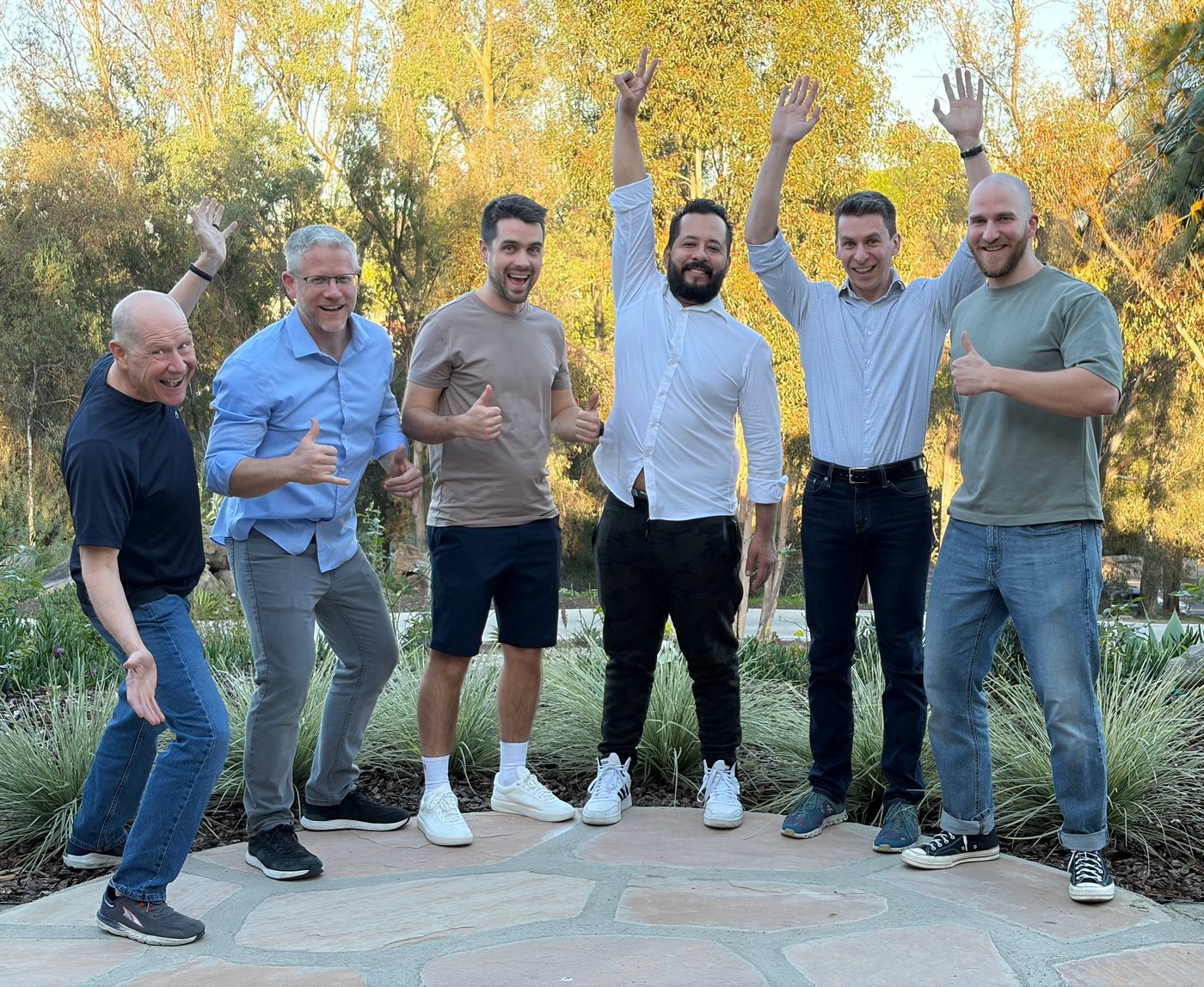 The DialStack team celebrating outdoors, six people with arms raised and thumbs up